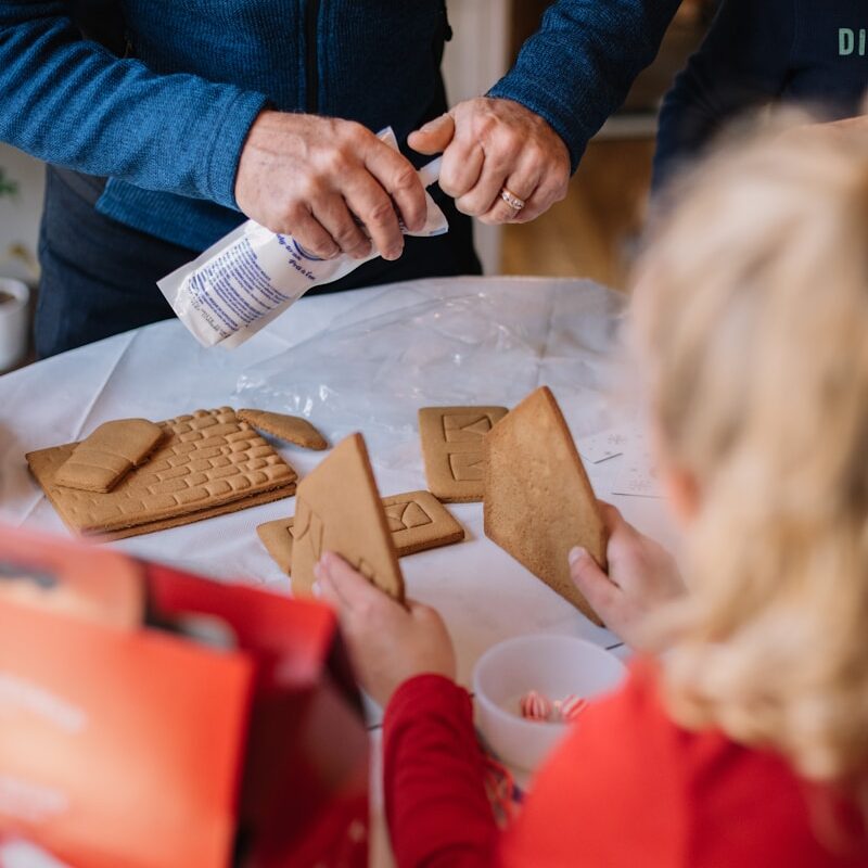 child holding crackers and another person holding whipped cream while standing